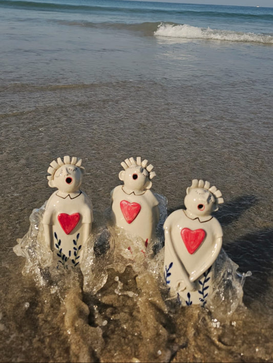 Three ceramic figures with red hearts on a beach with waves in the background